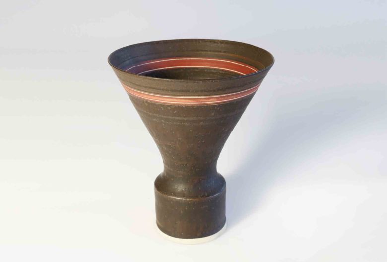 447 
Lucie Rie, Vase, 1971. Porzellan. Manganbraune, matte wellig strukturierte Glasur mit innen und außen umlaufendem roten Streifen und zwei hellen Sgraffito-Linien. H 17,6 cm, D 15,3 cm. € 20.000.
